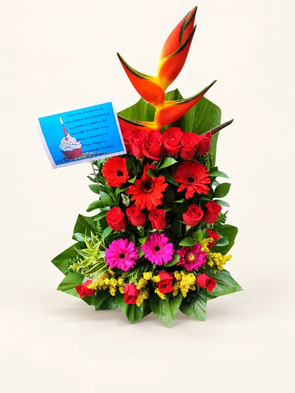 Caseta con heliconia, rosas rojas, gerberas rojas y rosadas y follaje tropical. Sobre fondo crema.
