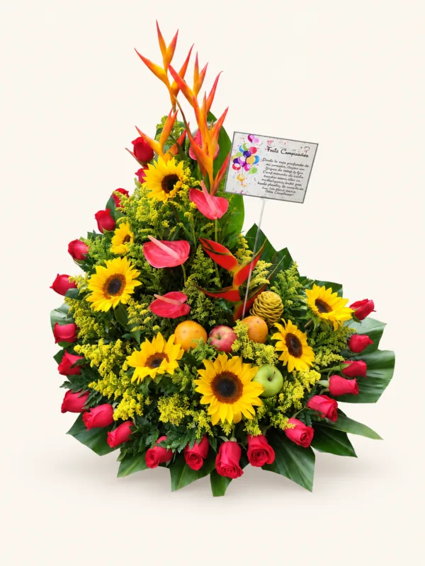 Arreglo de girasoles, rosas rojas, heliconias y anturios con frutas y follaje. Sobre fondo crema.