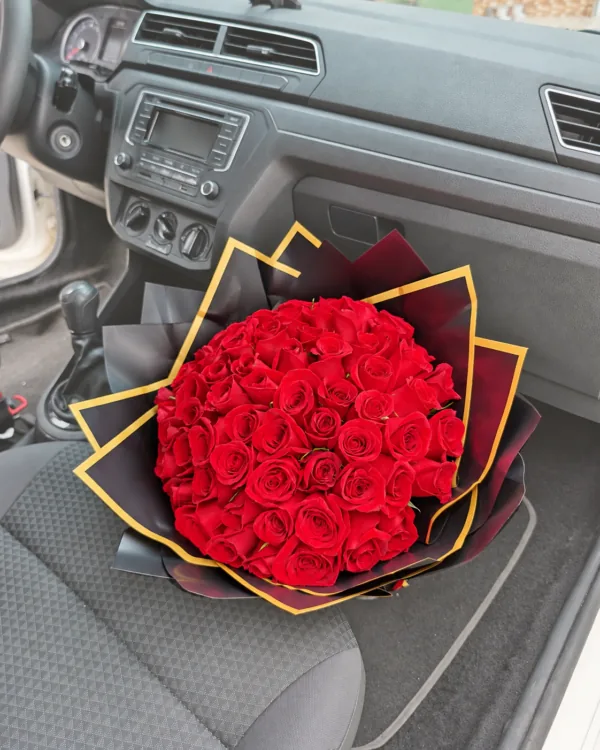 Bouquet de 48 rosas rojas en papel coreano rosado dentro de un vehículo, con retoque crema suave en el entorno en Pereira